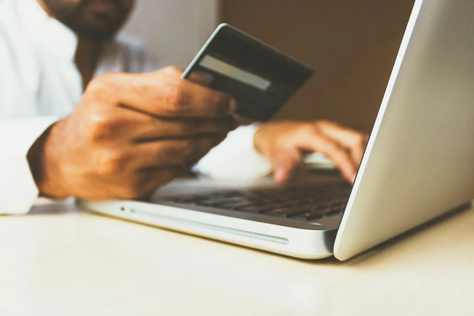 Hands holding a payment card in front of a laptop